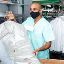 drycleaner with mask handing clean clothes to customer